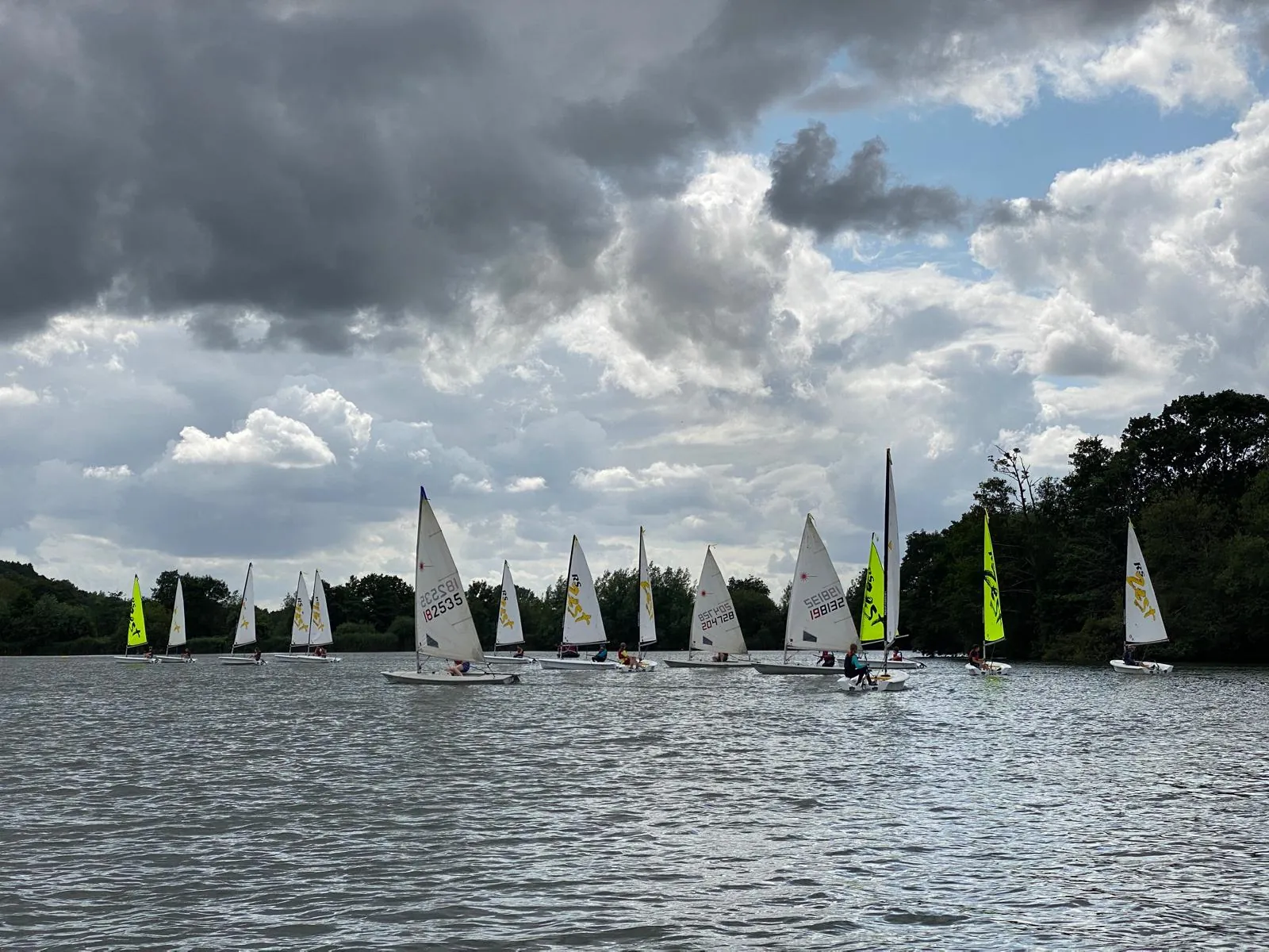 A fleet of sailing dinghies on the lake under dramatic skies